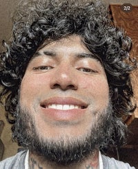 a man with curly hair and tattoos smiling